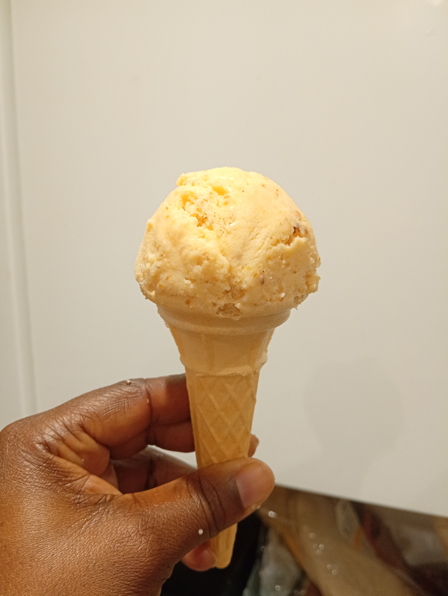 A single scoop of peach and ricotta ice cream in a wafer cone