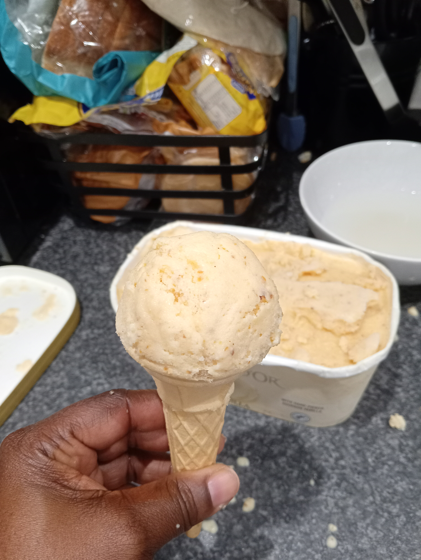 A scoop in a cone beside the open tub of peach and ricotta ice cream